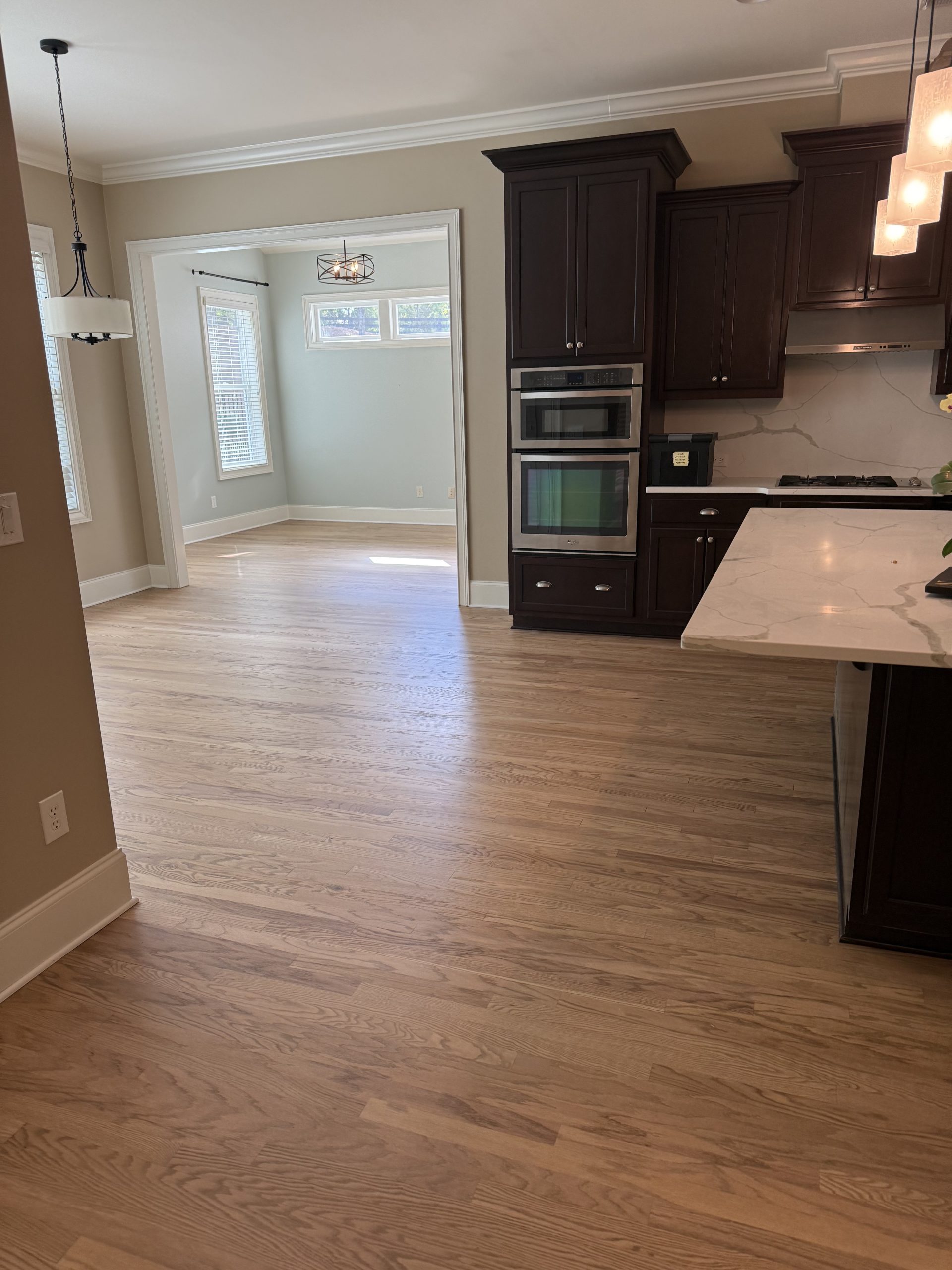 Red oak flooring running from a dining room through to a kitchen with dark cabinets
