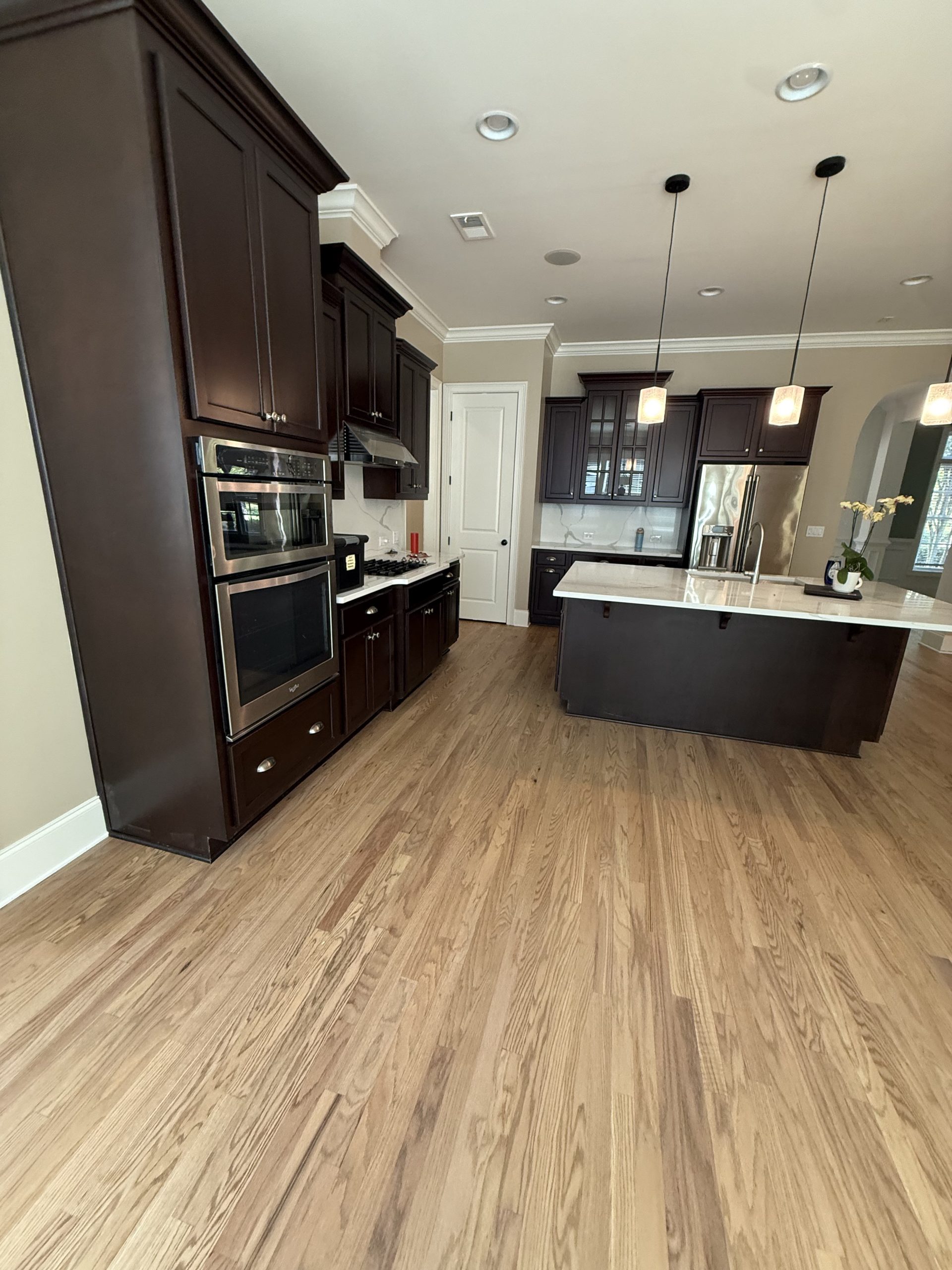 Wide-plank light oak flooring through an open kitchen and living area with dark cabinetry