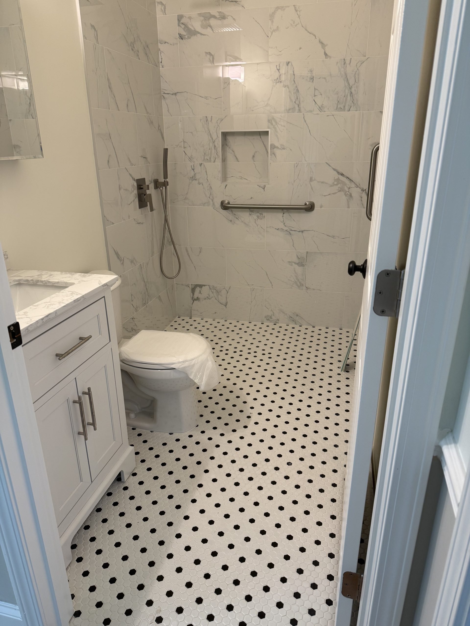 Bathroom with a black and white hexagon mosaic floor and a marble-look porcelain shower