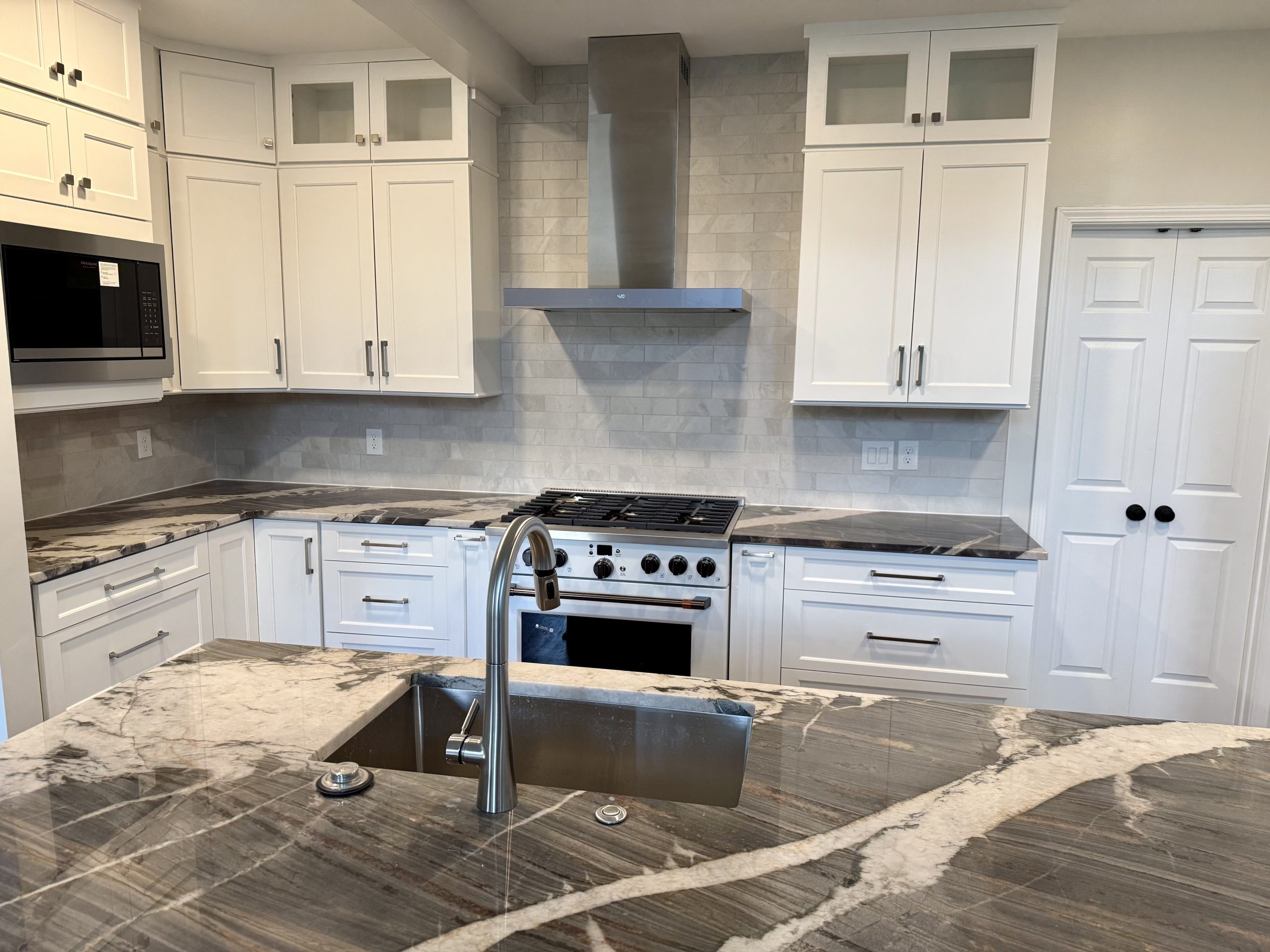 White shaker kitchen cabinets with a heavily veined stone island and countertop