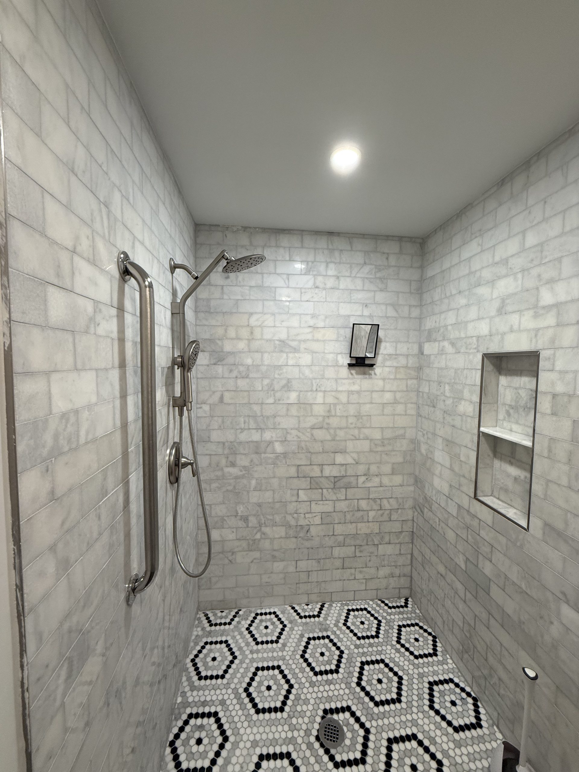 Marble-look subway tile shower with a hexagon mosaic floor and recessed niche