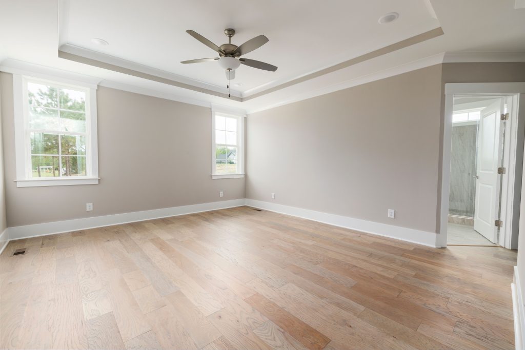 Open, modern bedroom with wooden floors and ceiling fan, ideal for staging.